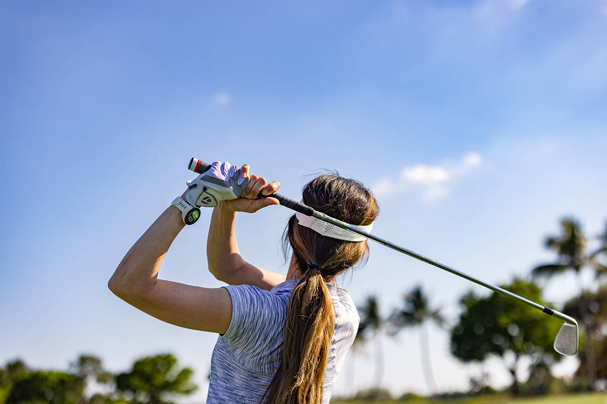 A female golfer from the waist up swinging a golf club on the course while wearing a white 42 mm Garmin Approach S70  golf watch