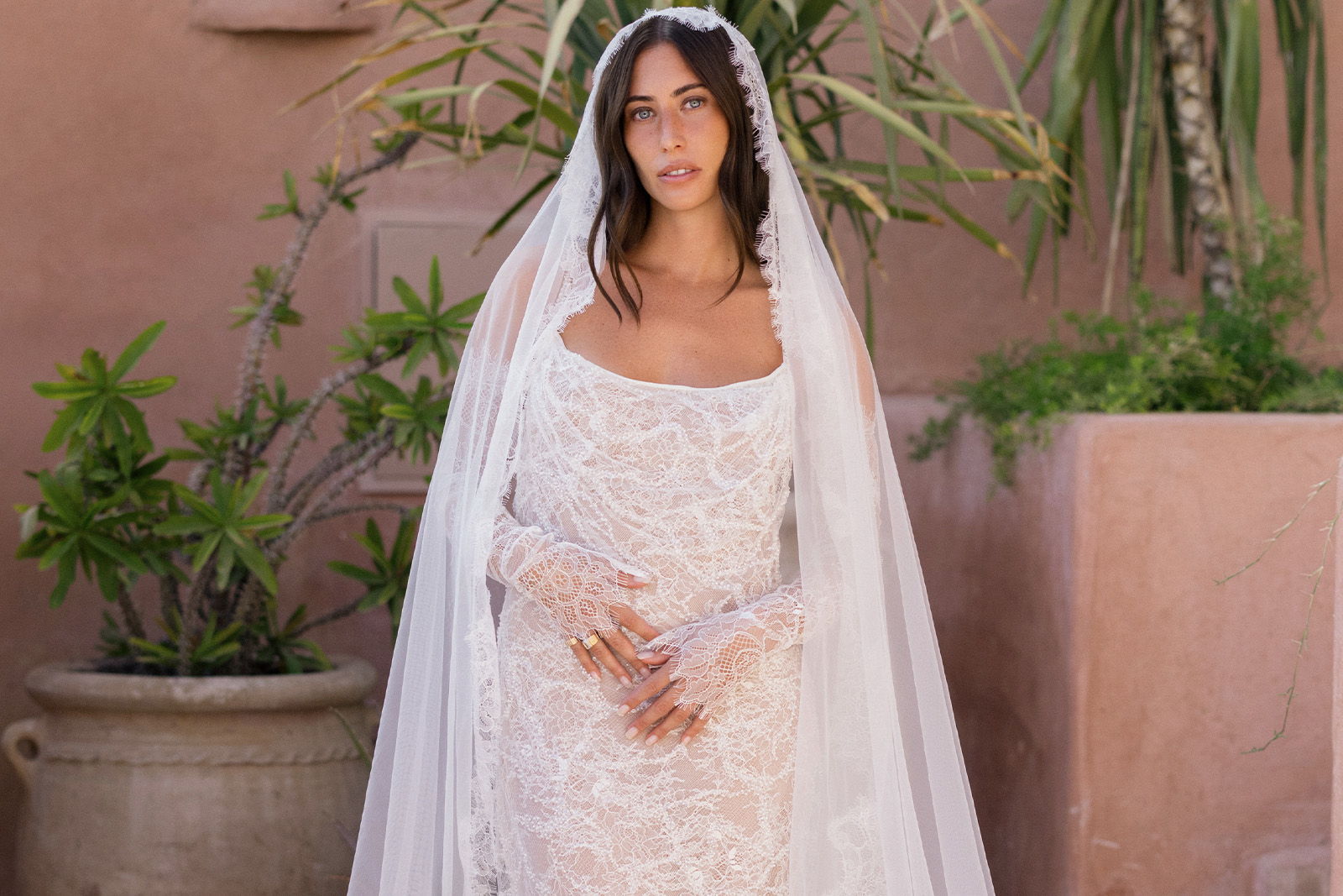 Bride in a white wedding dress with a veil, surrounded by greenery.