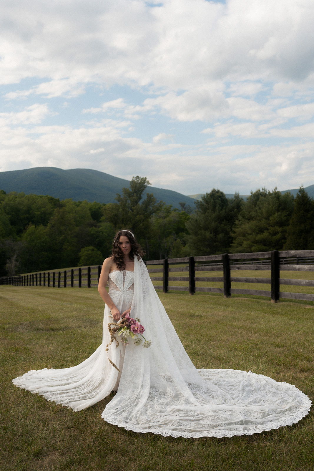 Bride in a flowing wedding dress holding flowers in a scenic outdoor setting.