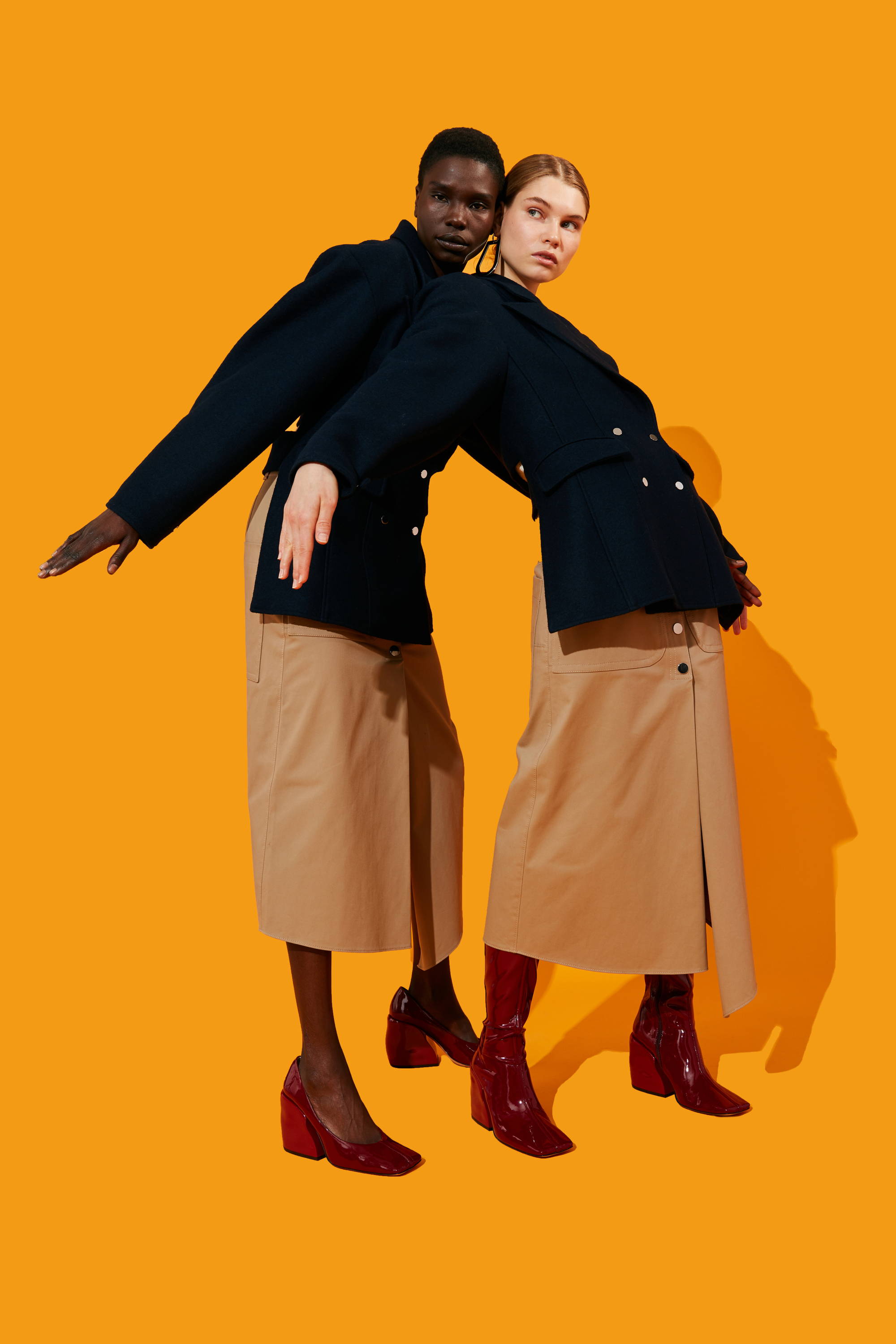 Two models in stylish outfits against an orange background.