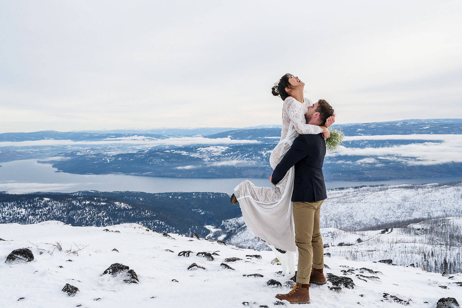 Groom, lifting the bride in the air, surrounded by snowy mountains