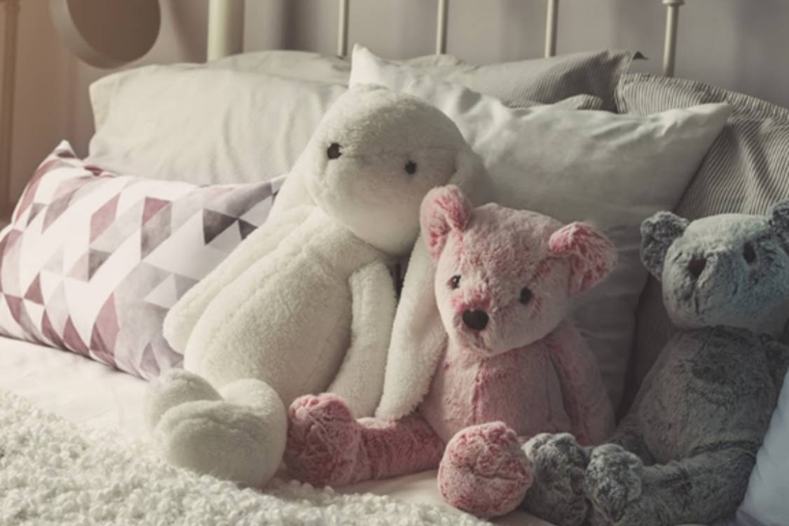 Knuffeldieren, zoals deze 3 knuffelberen op een bed, moeten regelmatig gewassen worden of 1 à 2 dagen in de vriezer worden bewaard als maatregel tegen huisstofmijtallergie.