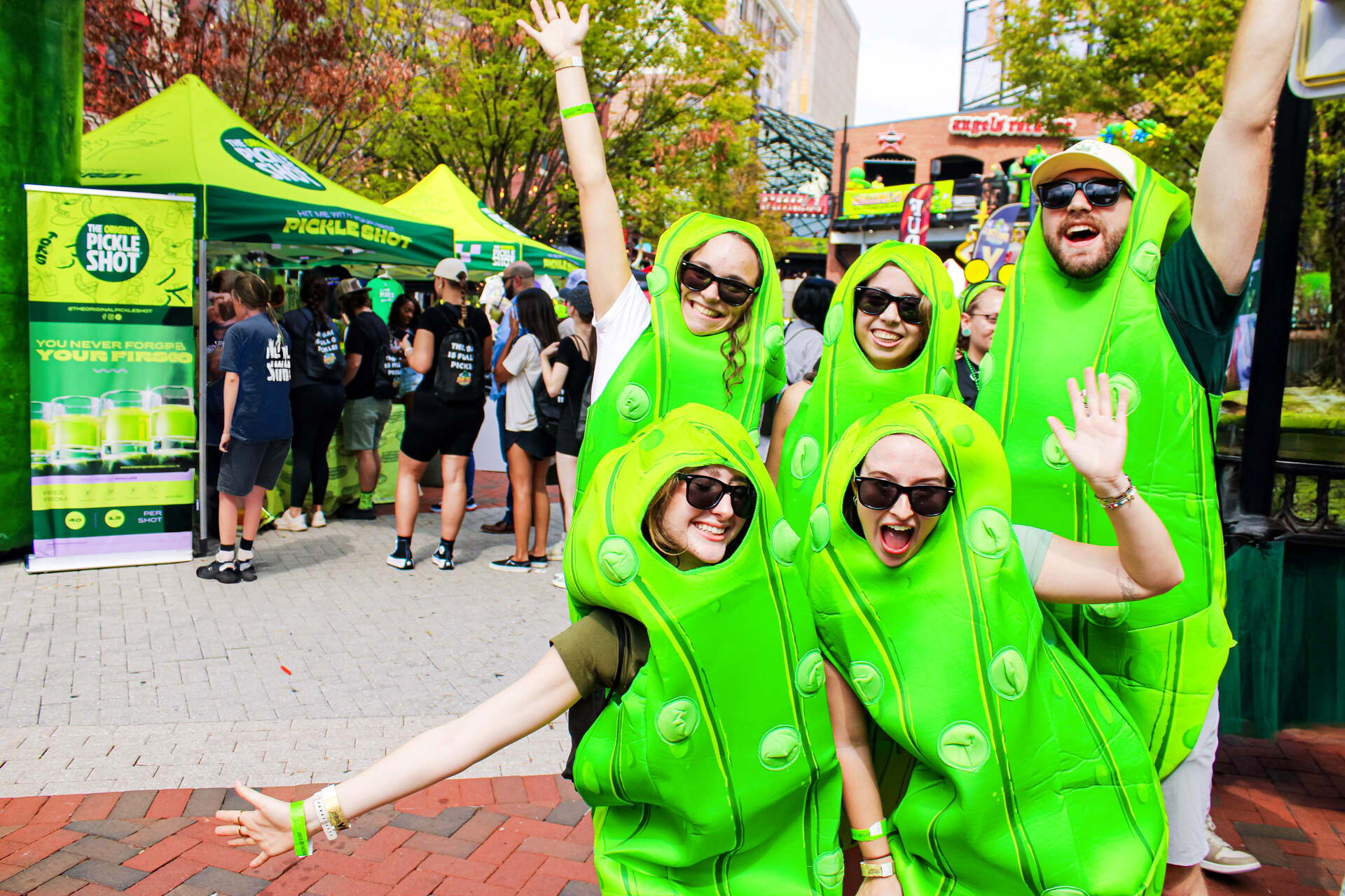 Friends in pickle costumes celebrating at The Original Pickle Shot booth at The Big Dill® pickle festival 2025 in Baltimore Maryland