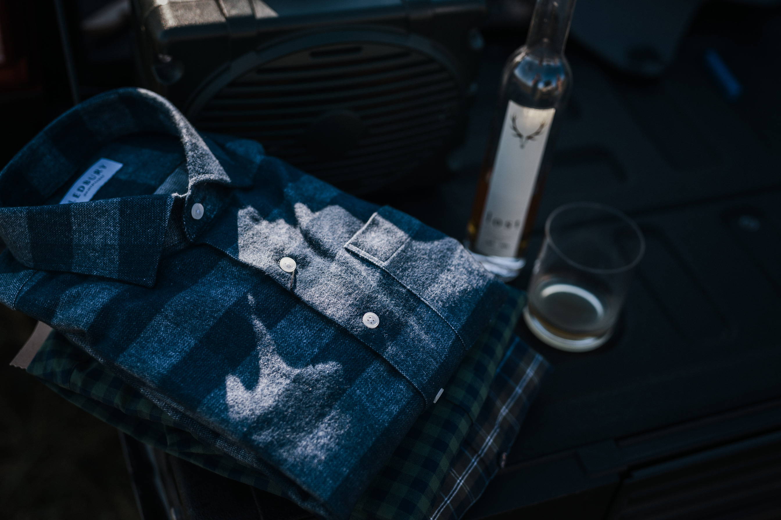 The Navy Randolph Custom shirt folded next to a bottle of Lost Whiskey.