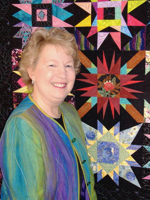 Photo of Carol Doak standing next to one of her paper pieced quilts
