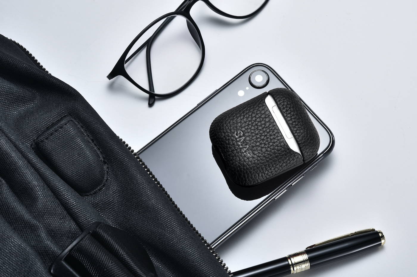 Black genuine leather airpods laying on iphone that is being compact into a bag