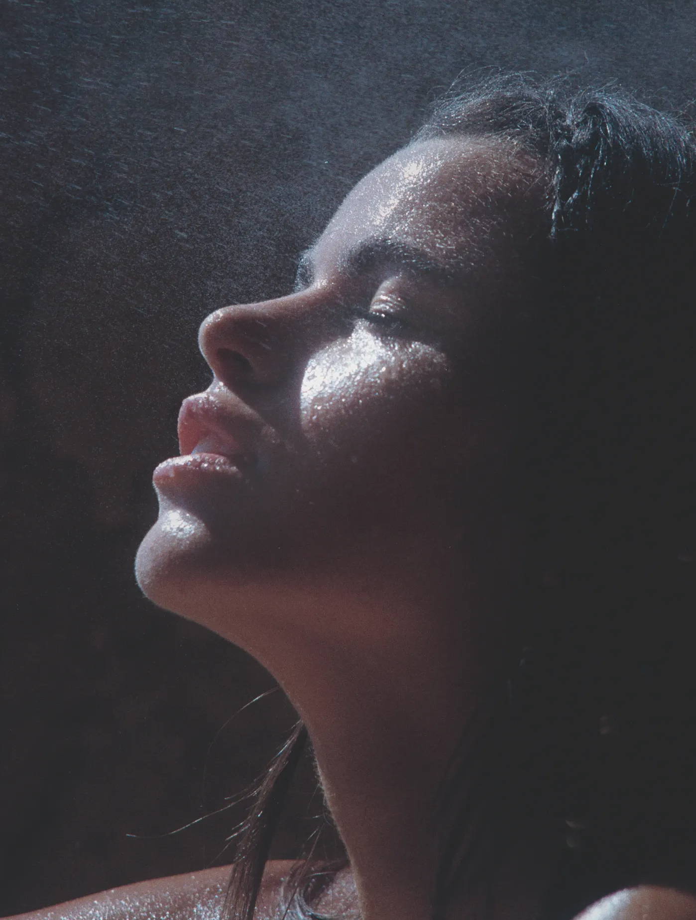 A person's face relaxing under a veil of mist against a dark background.
