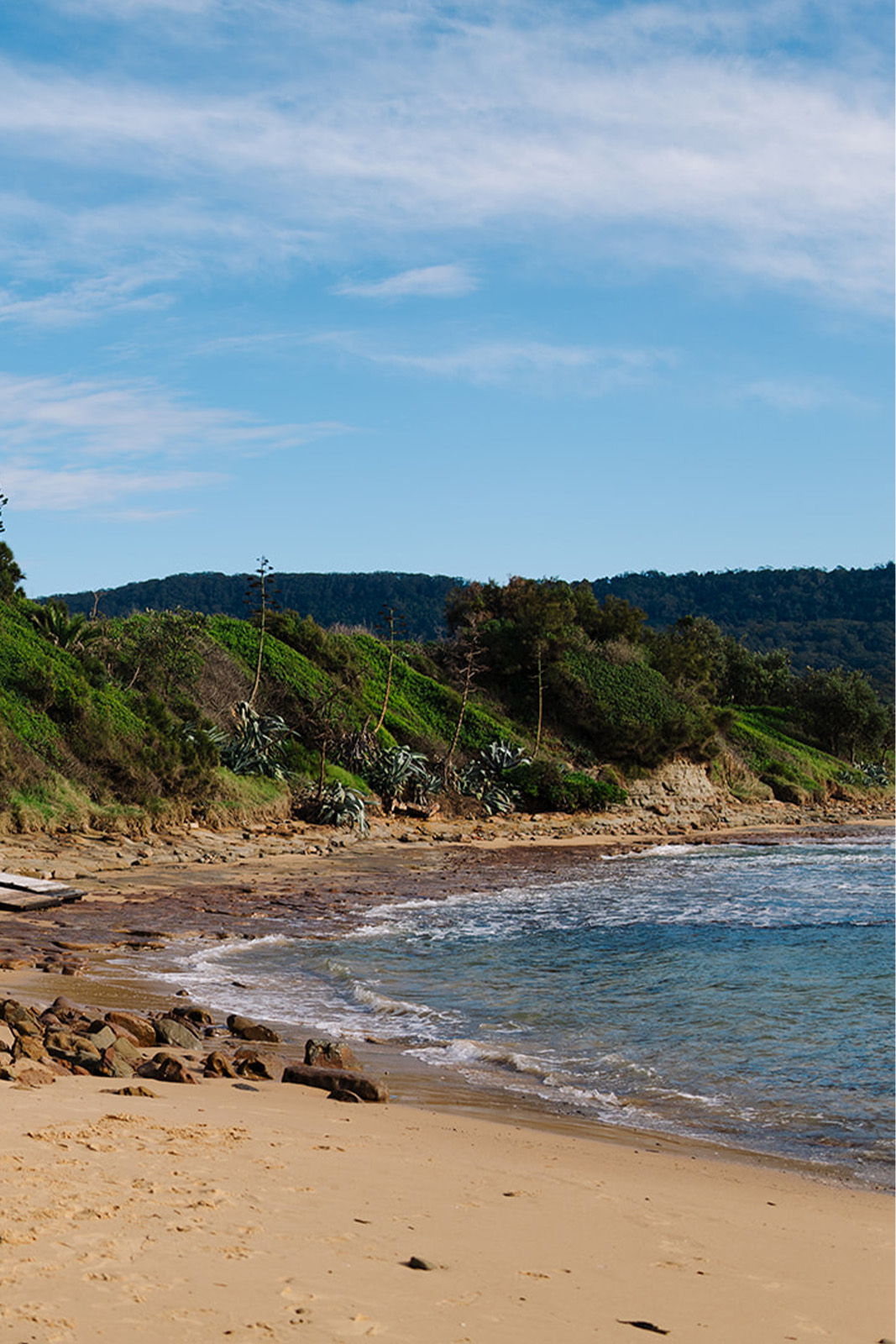 A serene beach with gentle waves and green hills in the background.
