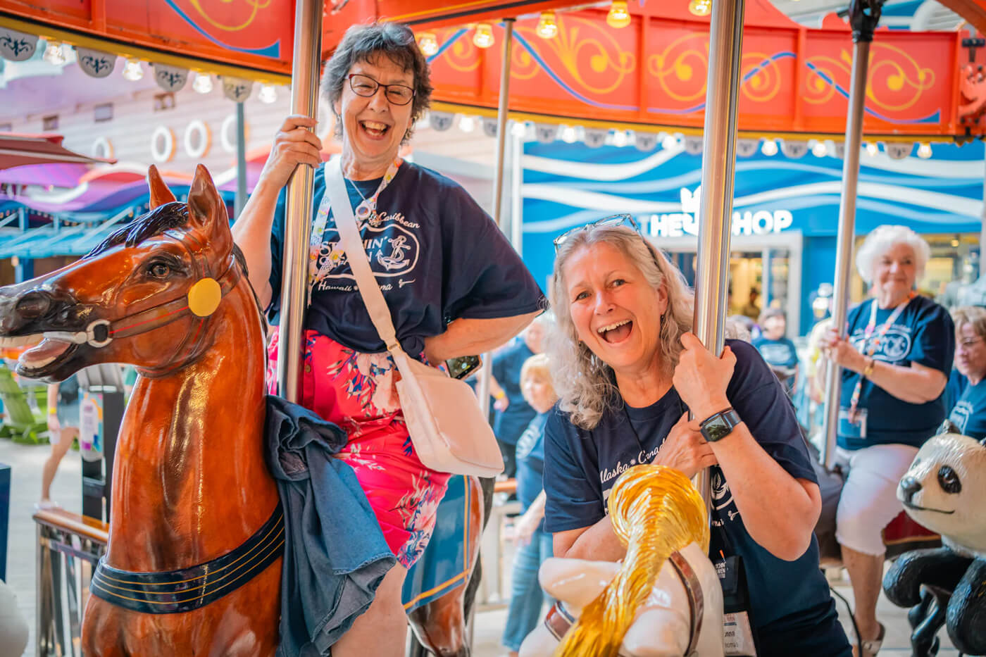Two women joyfully riding a carousel, smiling and holding onto the horses.