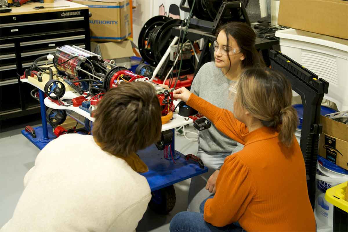Three people discussing a robotics project in a workshop.