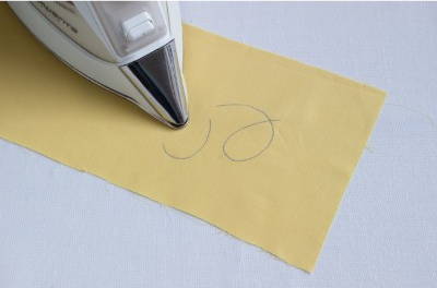 image of an iron erasing the blue fabric marking pen marks on a yellow piece of fabric