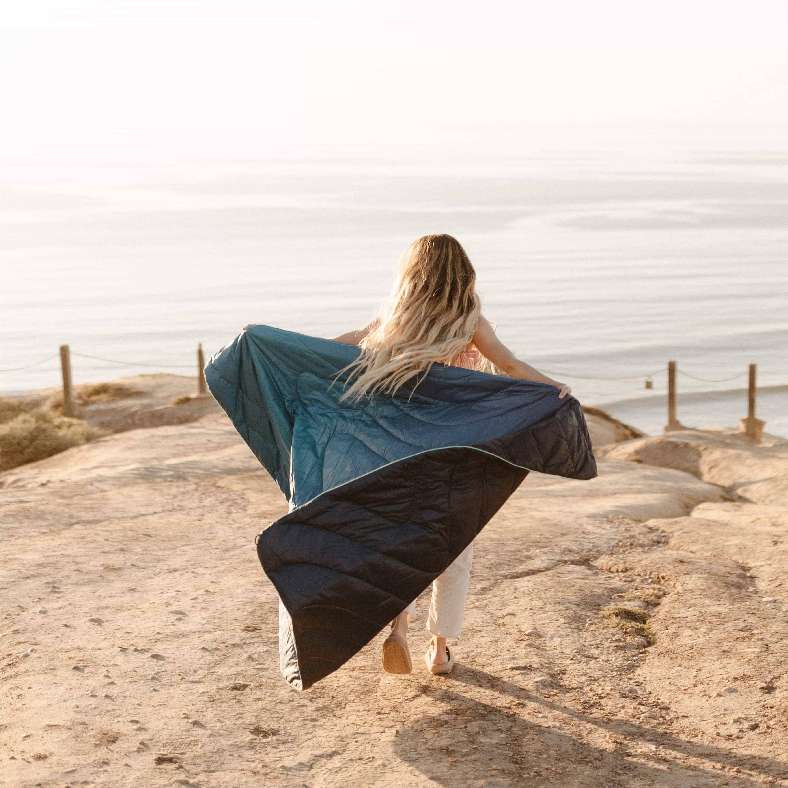 Woman Wrapped In Original Puffy Blanket Overlooking Cliff Above Ocean