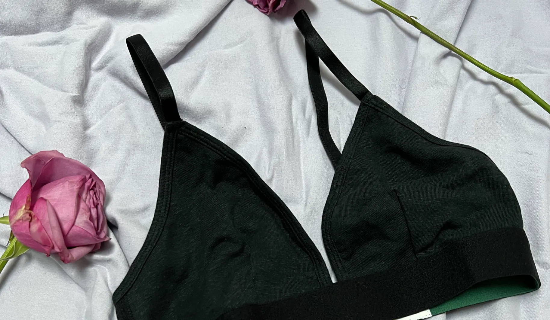 Photo of a black bralette laying on a white sheet framed by two pink roses