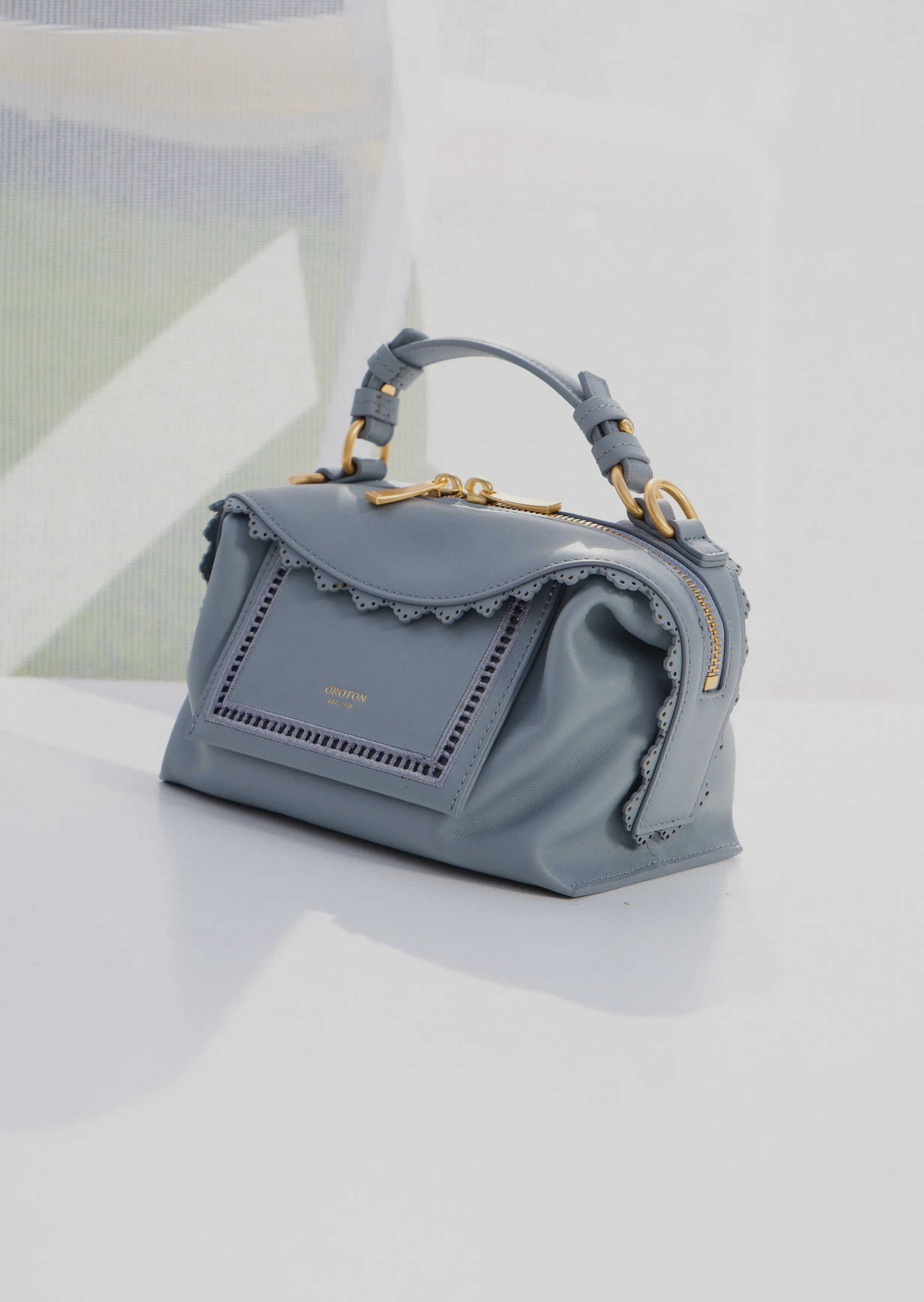 A stylish light blue handbag with a ruffled design and gold accents.