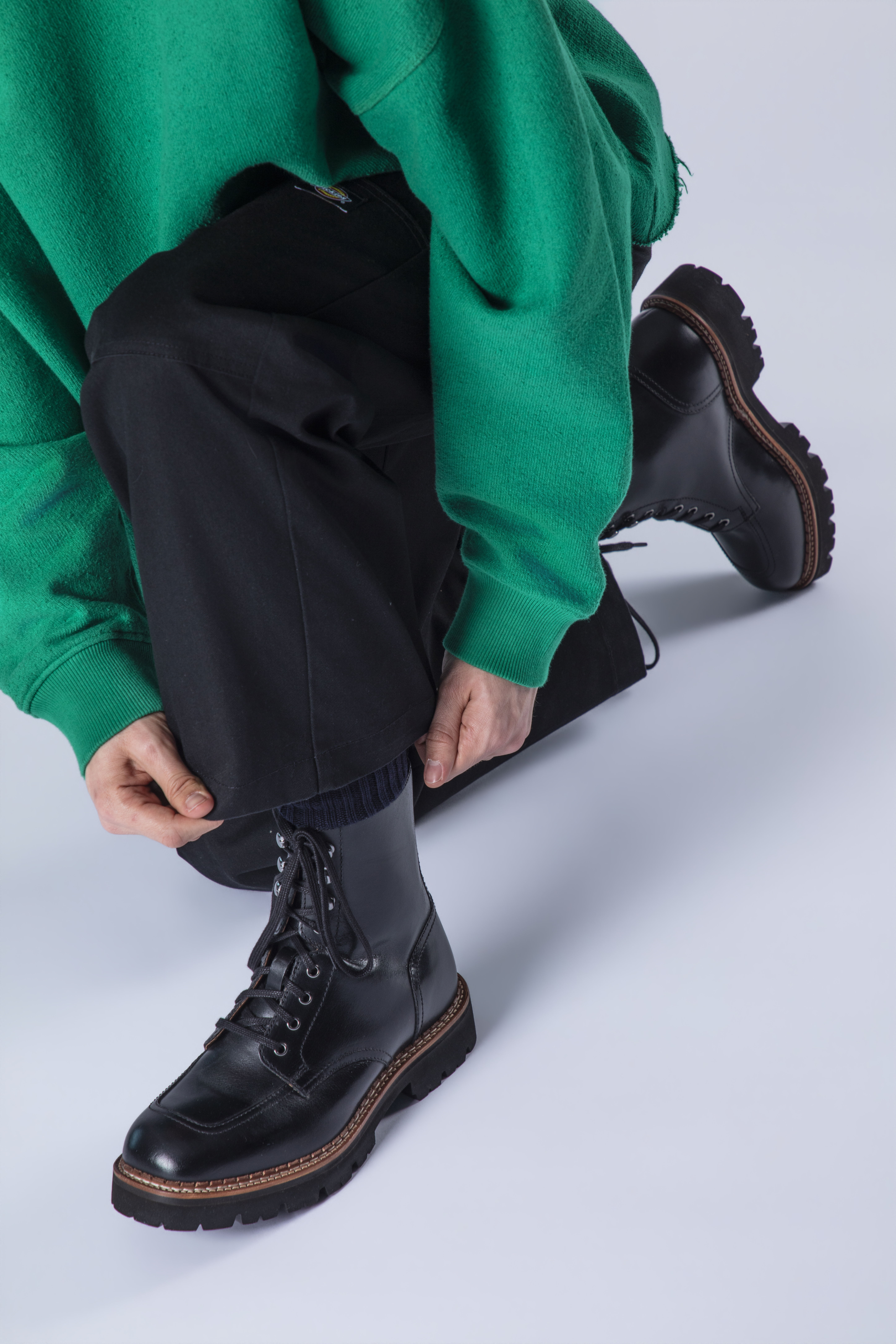 Person kneeling, tying laces on black boots, wearing a green sweater.