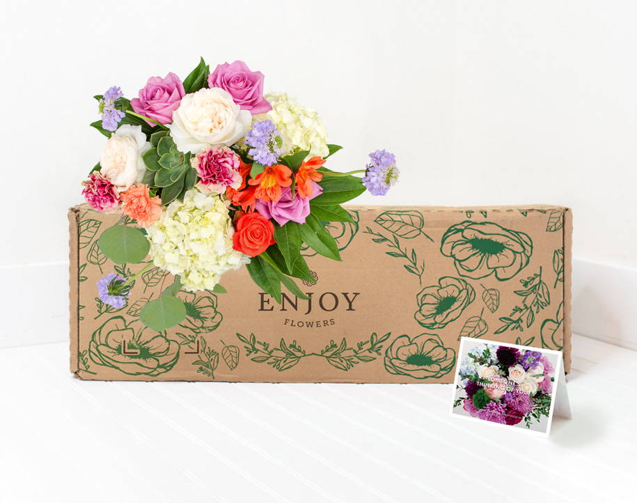 A bright bouquet of premium spring flowers from the Enjoy Flowers Signature Collection sits by a box and personalized card. 