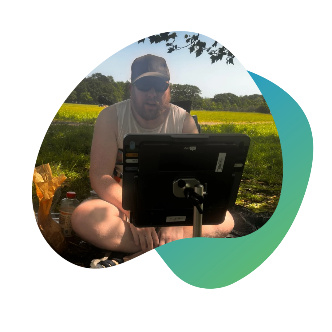 Person sitting outdoors, using a Grid Pad with Evo in a green field.