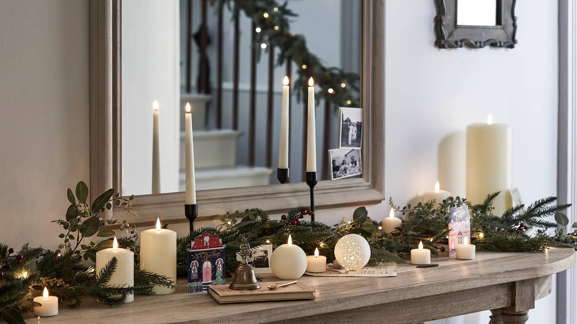 A mantlepiece with candles, a garland and Christmas decorations.