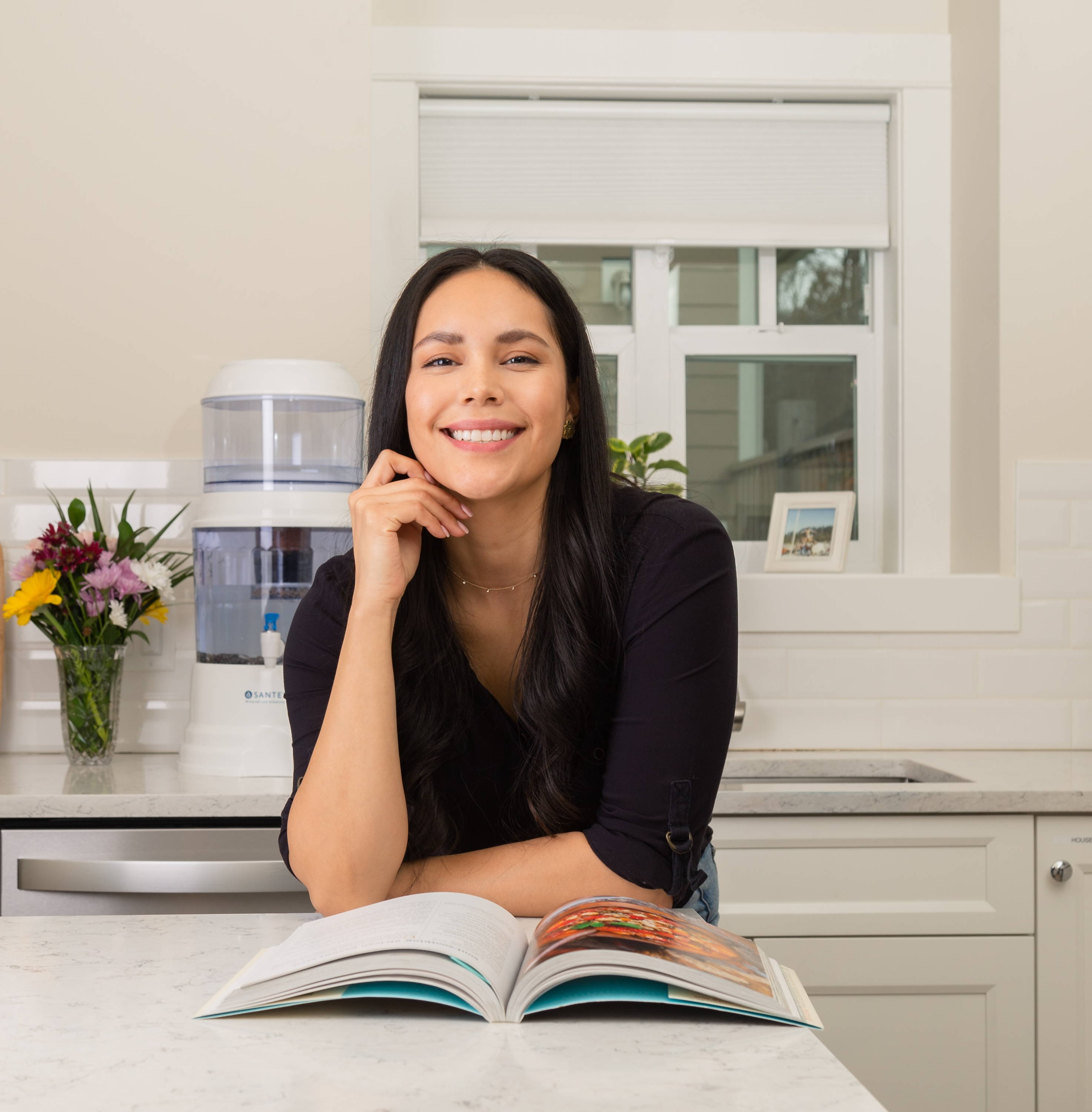 A woman smiling while reading a cookbook in front of her Santevia Gravity Water System
