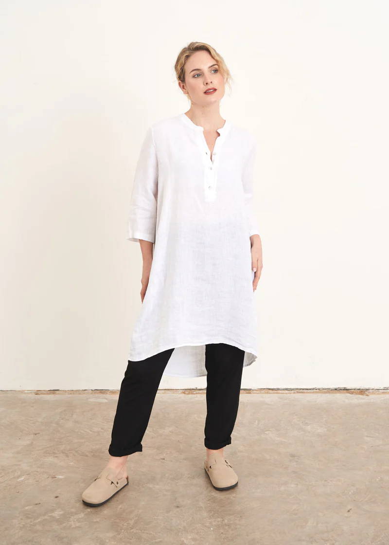 A model wearing a long white linen tunic with black trousers and off white clogs