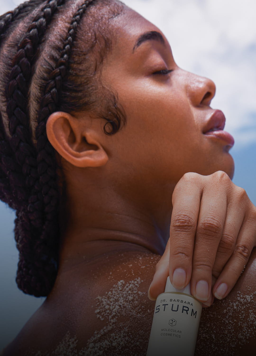 Woman with braided hair holding a skincare product, eyes closed, serene expression.