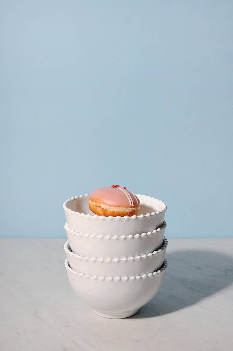 A stack of four pearl white cereal bowls with a pink glazed donut in the top one.