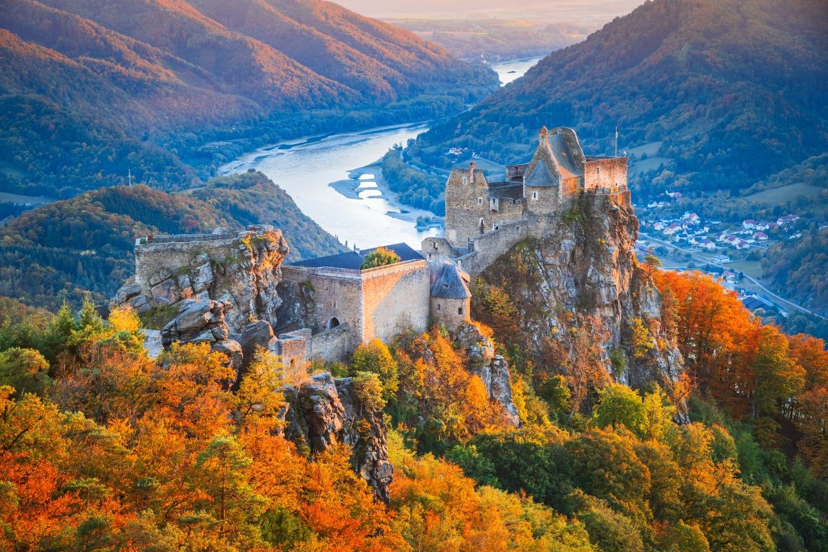Scenic view of a castle amid autumn foliage and a river.