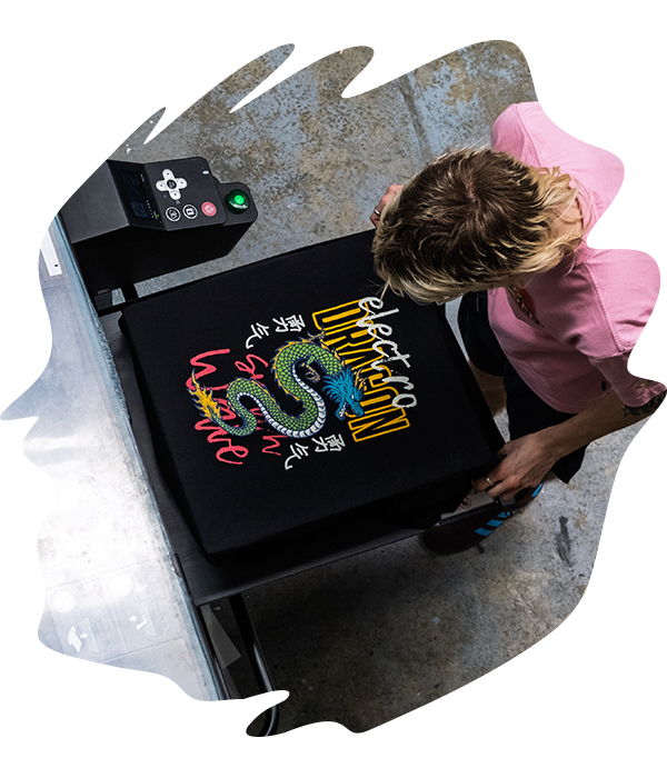 Overhead view of a person operating a DTG printer on a black t-shirt featuring a colourful dragon design